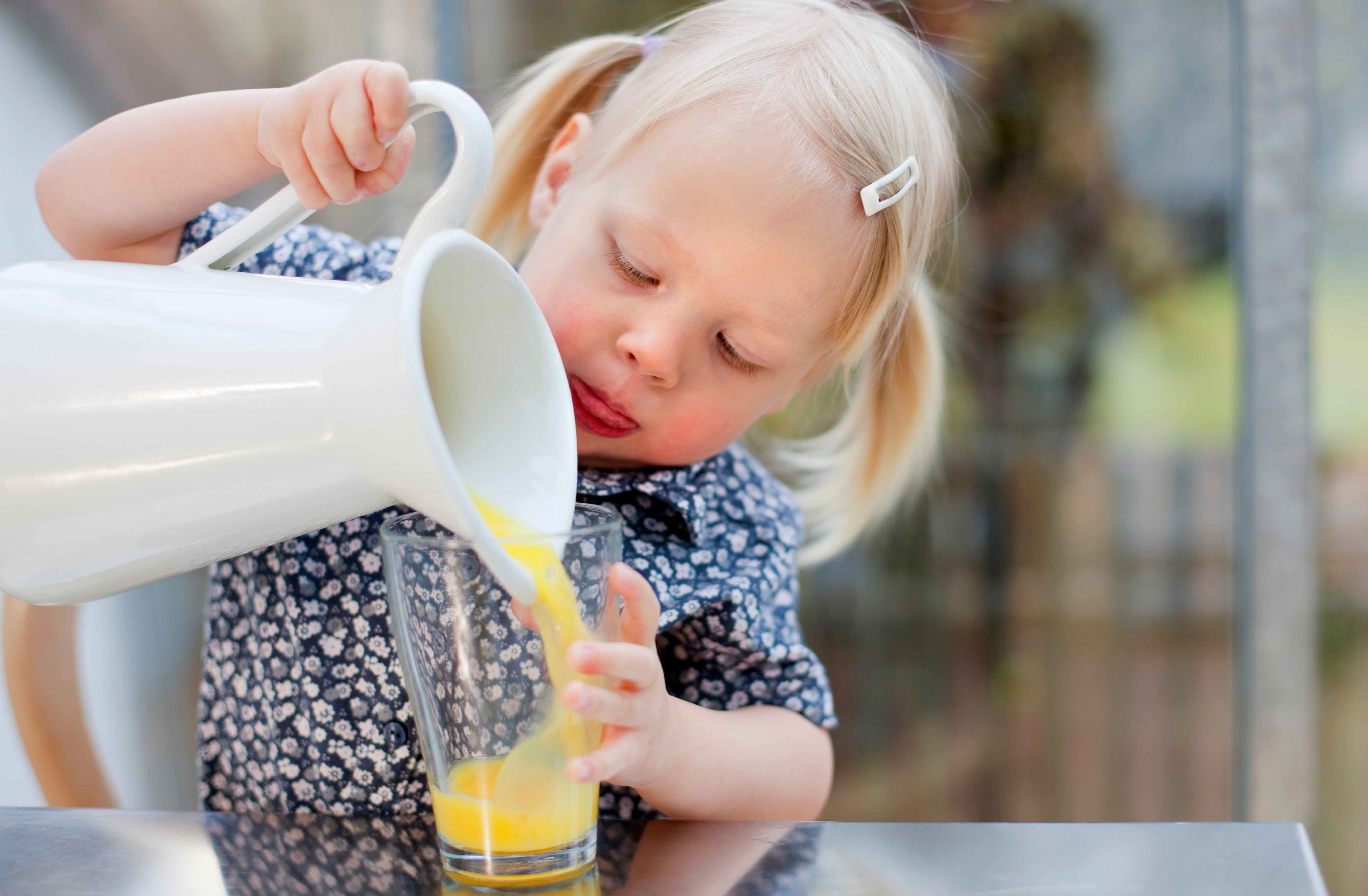 toddler girl pouring a glass of juice 